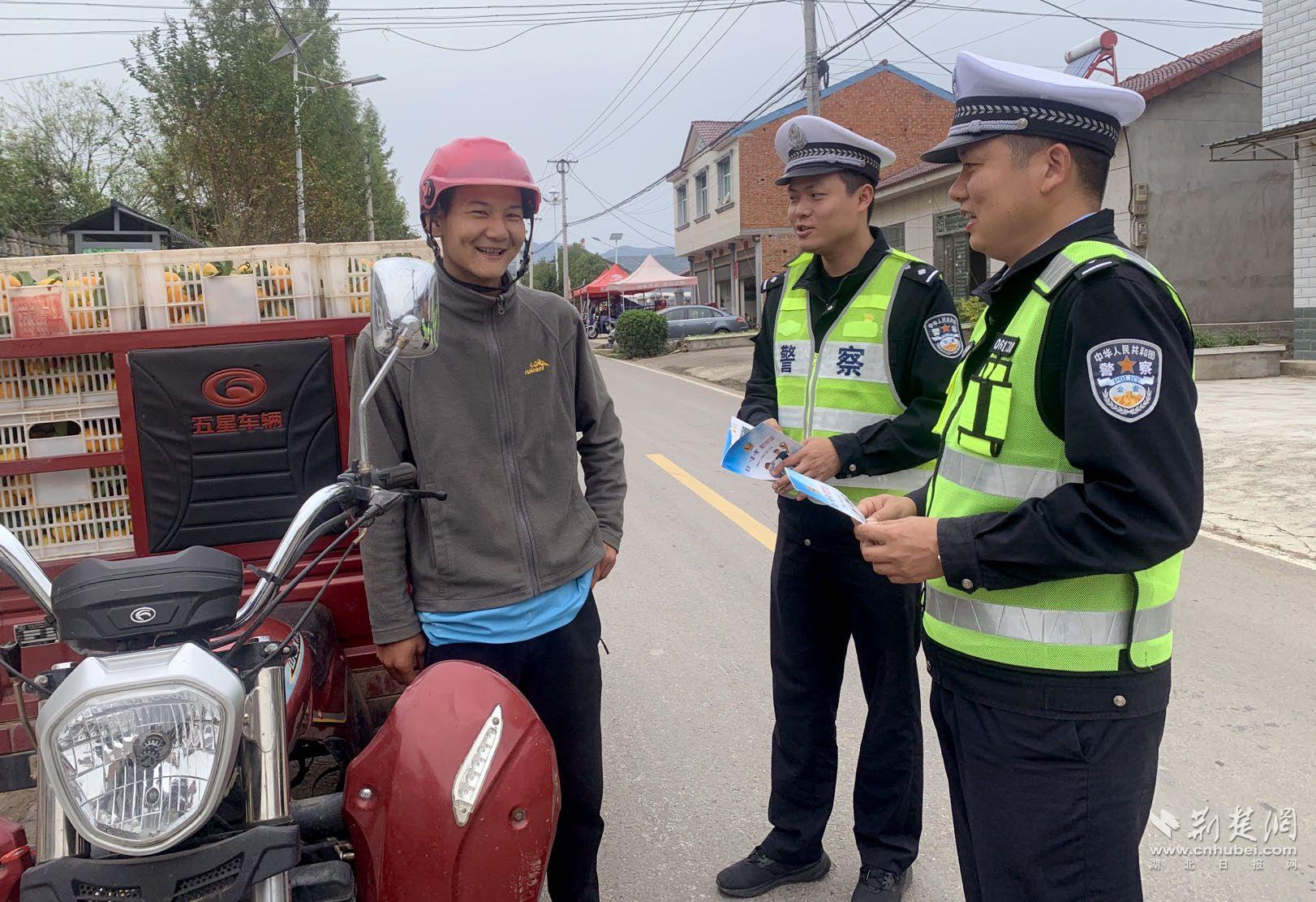 派出所教导员郑挺带领民警和辅警指挥着车辆运行，提醒驾驶员安全行车。民警提醒果农正确佩戴安全头盔。（通